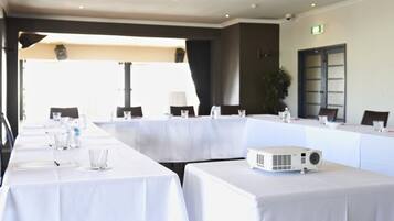 A conference room with long tables, chairs, a projector, and a plant.
