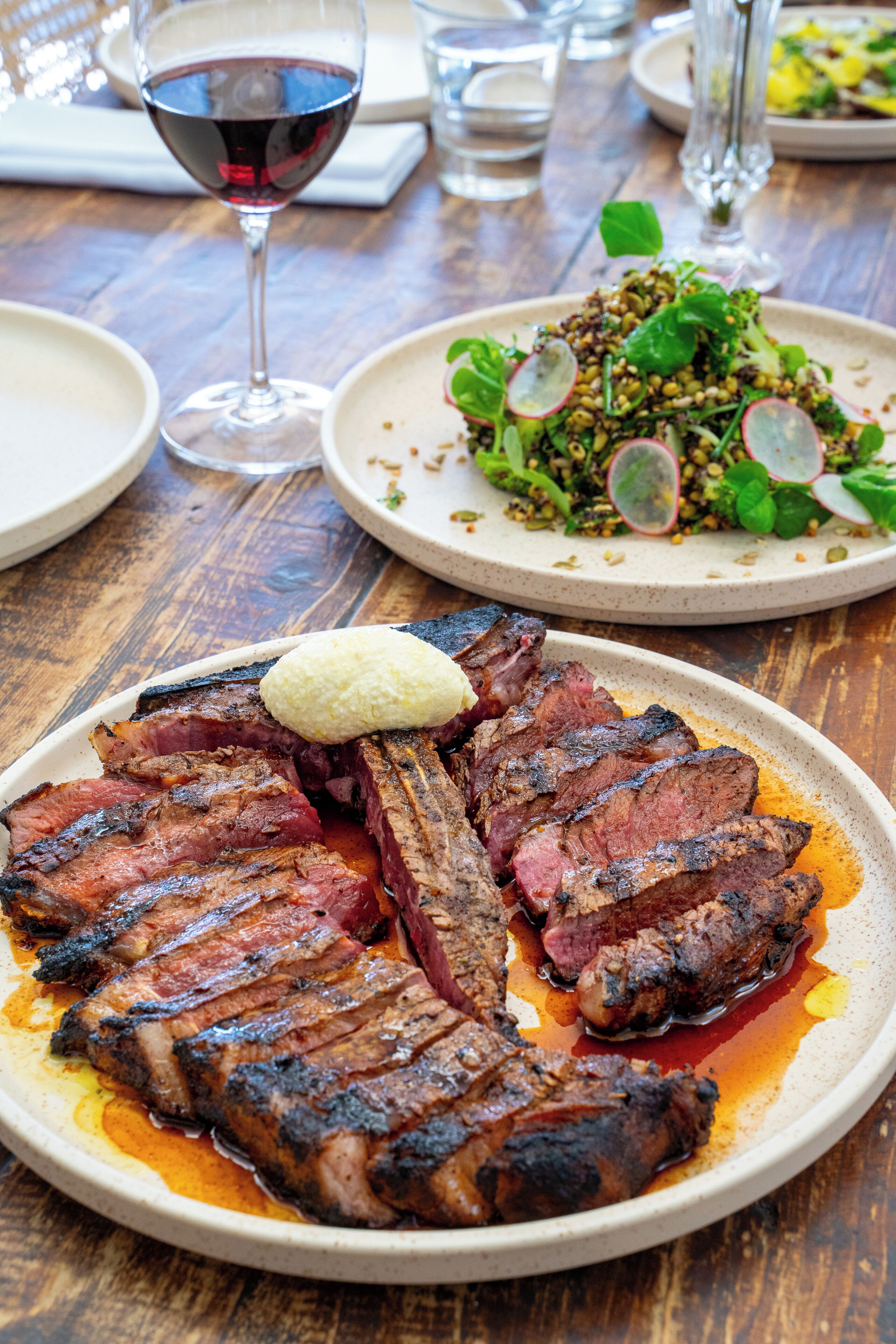 Una mesa de comedor con un plato de carne, una copa de vino tinto y una ensalada.