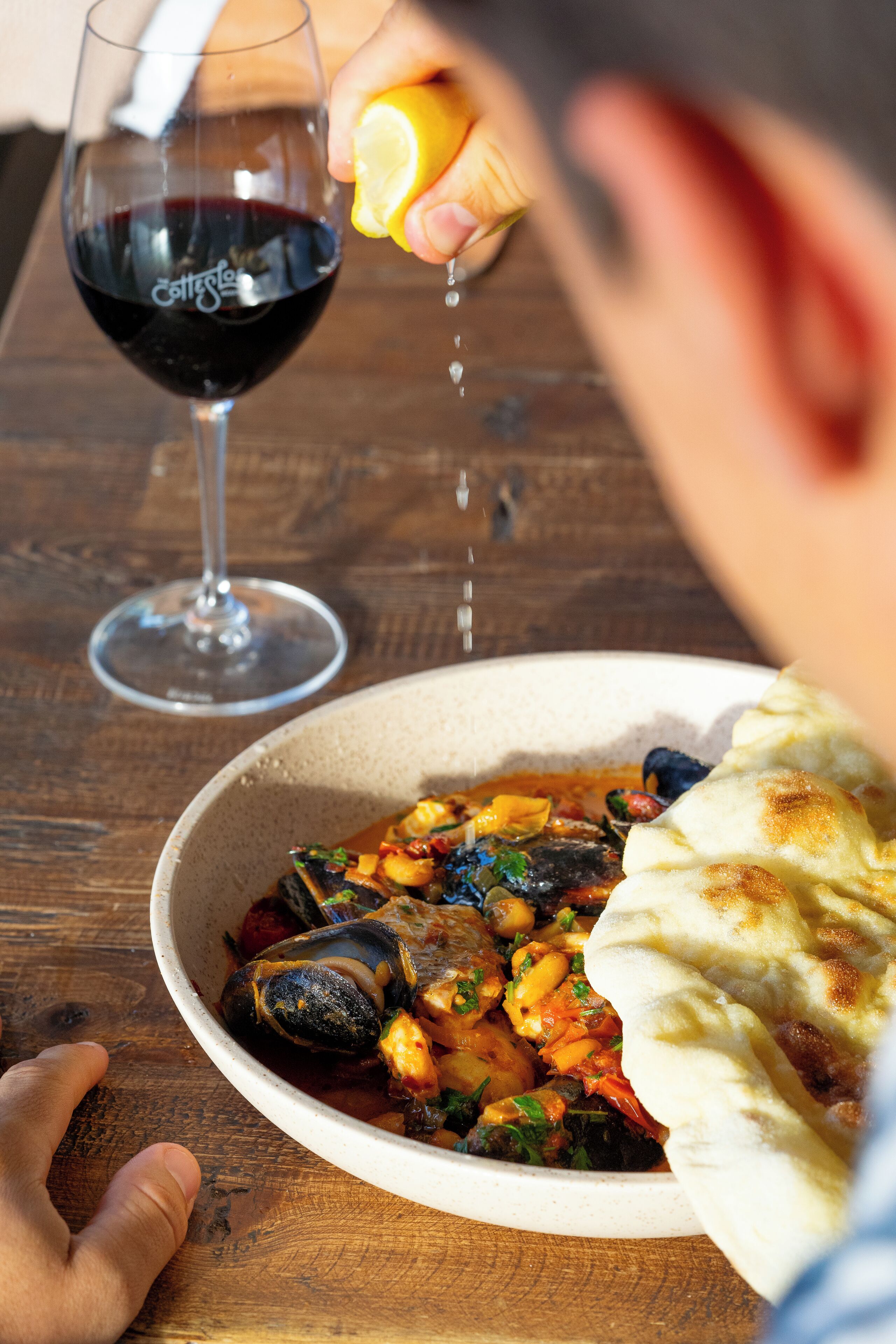Un cuenco de guiso de mariscos con pan sobre una mesa de madera.