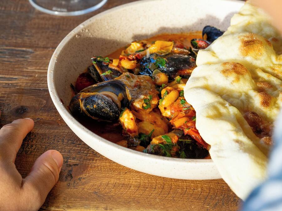 Un cuenco de guiso de mariscos con pan sobre una mesa de madera.
