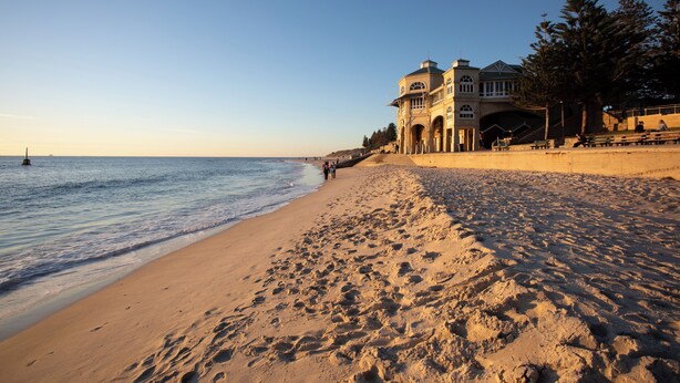 A beach with a building featuring arched walkways and a large staircase leading to an upper level. - Cottesloe Beach Hotel (Cottesloe)