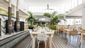 A spacious indoor dining area with a long wooden table, white chairs, and a modern ceiling fan. - Cottesloe Beach Hotel (Cottesloe)
