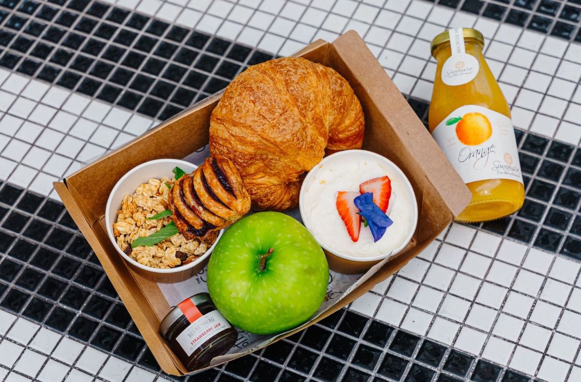 A breakfast tray with a croissant, yogurt with strawberries, granola, an apple, and a bottle of orange juice.