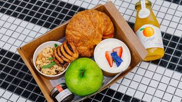 A breakfast tray with a croissant, yogurt with strawberries, granola, an apple, and a bottle of orange juice.