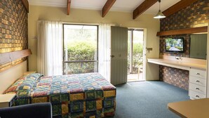 A bedroom with a bed, a desk, a dresser, and a television. There is a window with curtains and a door leading outside. - Pinnacle Holiday Lodge (Halls Gap)