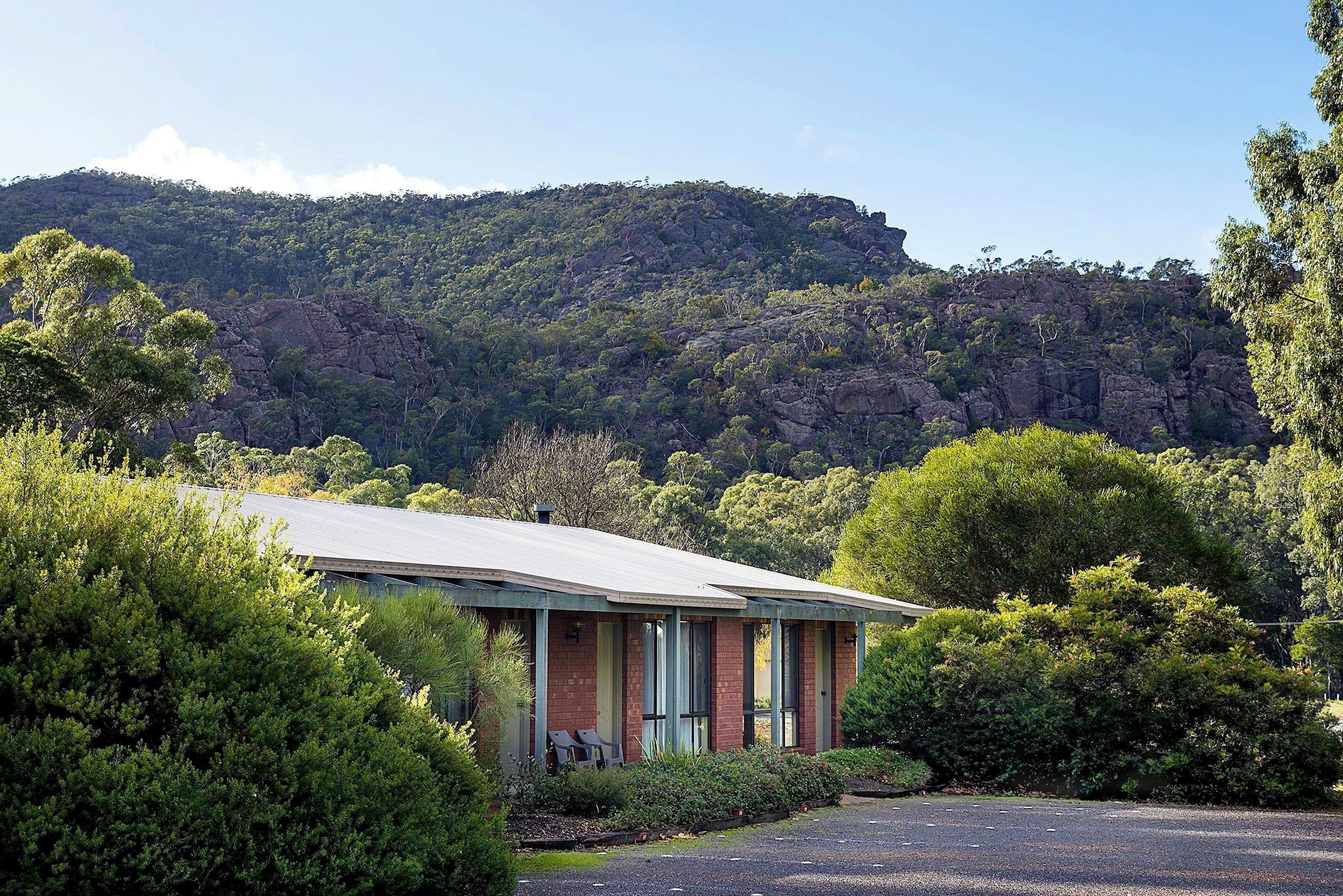 A building with a flat roof, surrounded by dense green foliage and a rocky hill in the background.