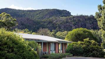 A building with a flat roof, surrounded by dense green foliage and a rocky hill in the background.