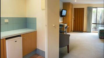 A compact kitchen with a built-in fridge, a dining area with a table and chairs, a TV mounted on the wall, and a sliding door leading to a balcony.