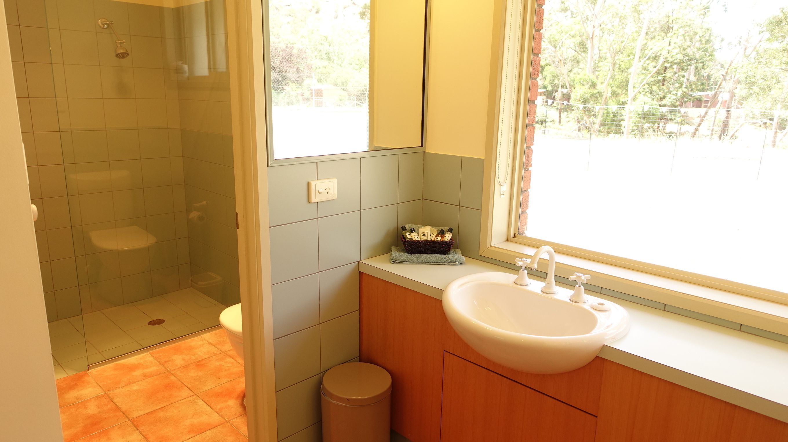 Ein Badezimmer mit Dusche, Toilette, Waschbecken und einem Fenster mit Blick ins Freie.