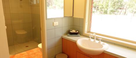 Ein Badezimmer mit Dusche, Toilette, Waschbecken und einem Fenster mit Blick ins Freie.
