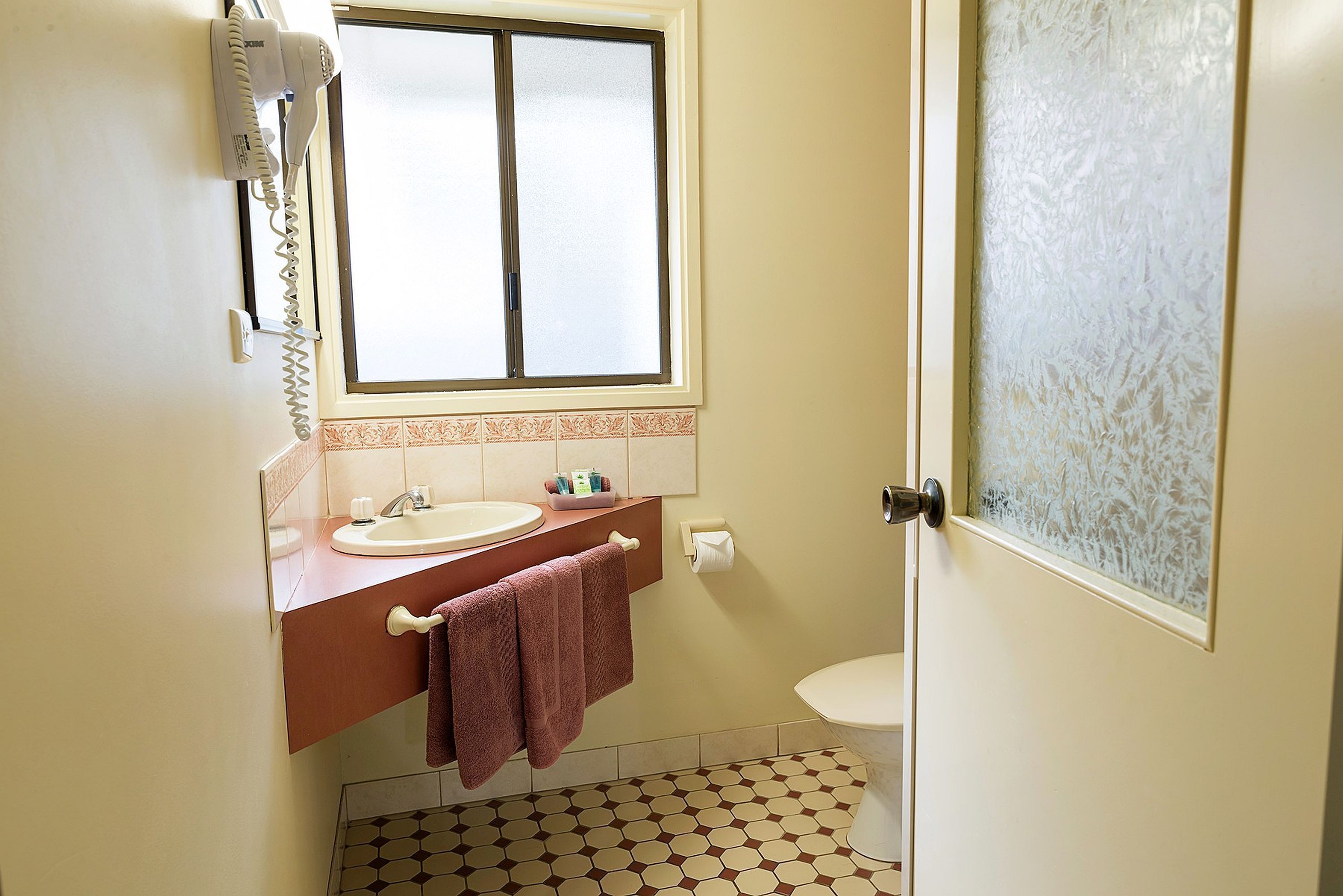 A bathroom with a sink, mirror, and a window above it.