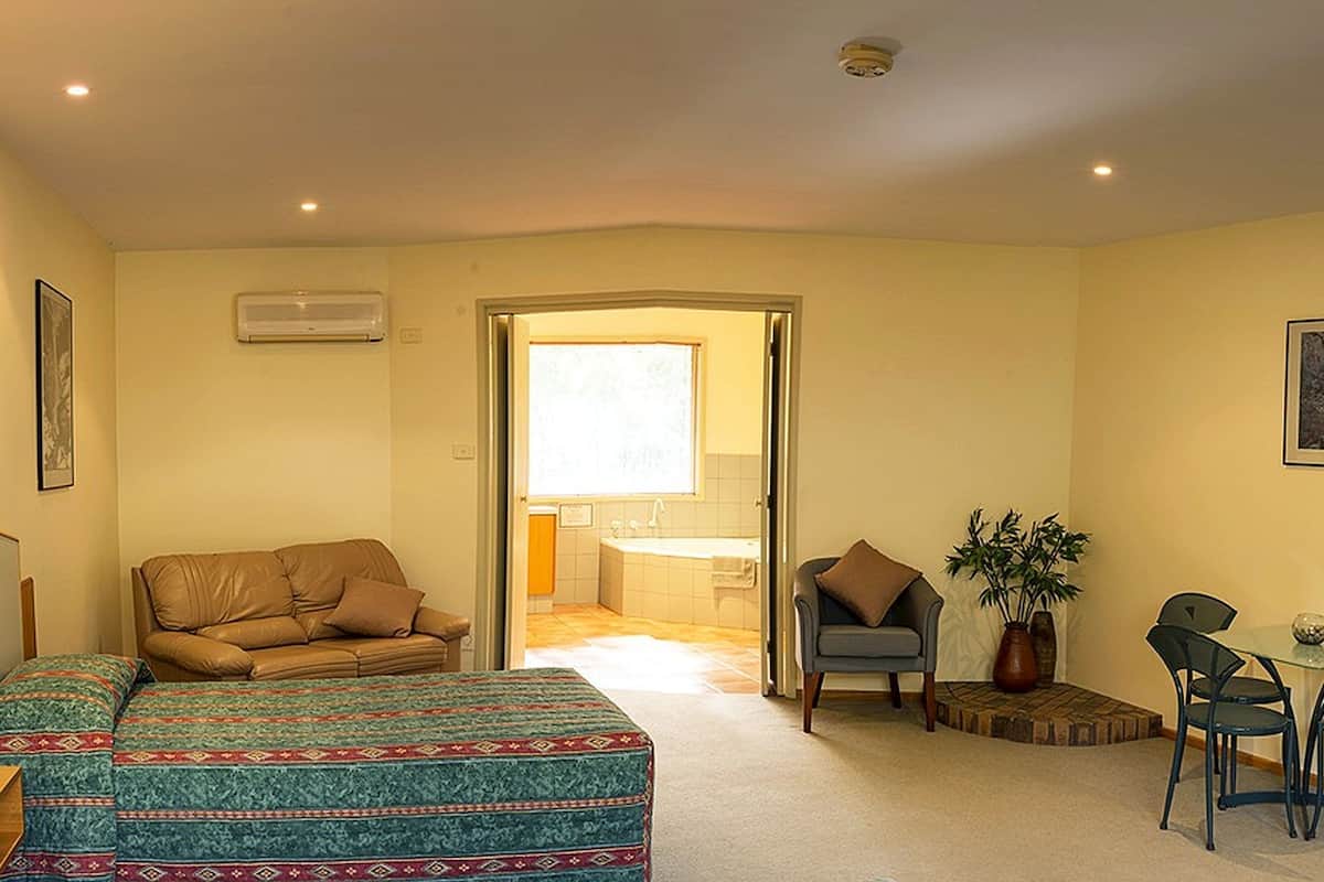 Ein Hotelzimmer mit Bett, Schreibtisch, Stuhl, Sofa, Fernseher und einem durch eine offene Tür einsehbaren Badezimmer.