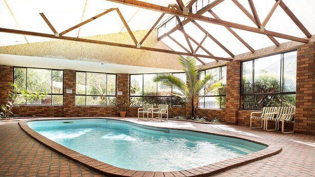 An indoor swimming pool with brick flooring, large windows, and wooden beams. - Pinnacle Holiday Lodge (Halls Gap)