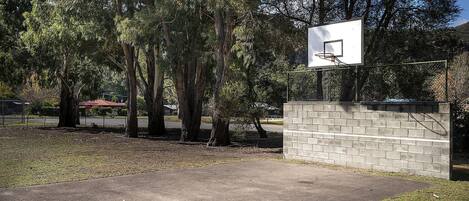 A basketball court with a concrete surface, surrounded by trees and a brick wall.