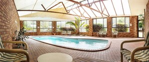 Una piscina interior con suelo de ladrillo, rodeada de ventanas y sillas.