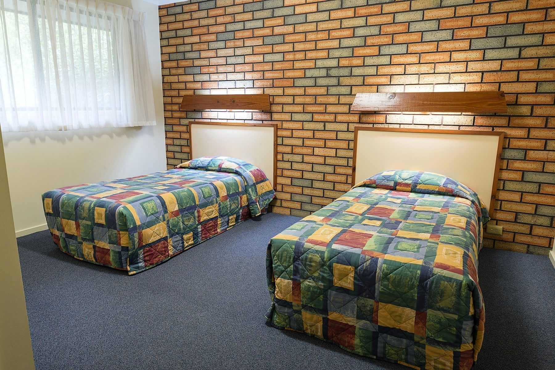 Une chambre avec deux lits, chacun recouvert d’une couverture aux couleurs vives, le tout adossé à un mur de briques doté d’un éclairage intégré.