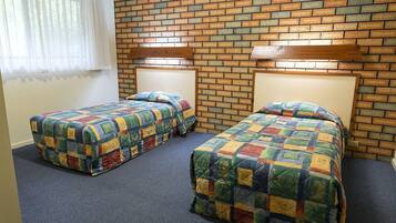 Une chambre avec deux lits, chacun recouvert d’une couverture aux couleurs vives, le tout adossé à un mur de briques doté d’un éclairage intégré.