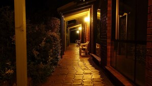 A brick pathway leading to a building with a covered porch and two chairs. - Pinnacle Holiday Lodge (Halls Gap)