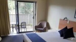 Une chambre d’hôtel avec un grand lit, une chaise et une table près d’une porte-fenêtre coulissante.