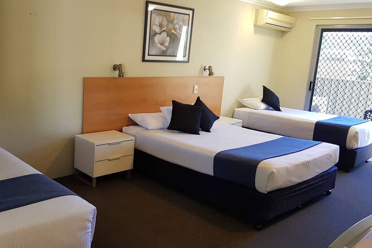 Hotellihuone, jossa on kaksi erillistä sänkyä, puinen pääty, yöpöytä ja seinällä oleva kehystetty kuva.