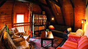 Acogedor interior de cabaña de troncos con techo de madera, una estantería, un sofá, un sillón y una mesa de centro.