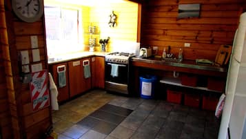 Una cocina con paredes de madera, estufa, pileta y un reloj.