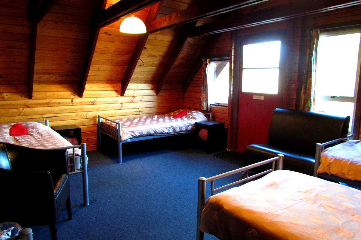 A cozy cabin with a sloped ceiling, a single bed, a chair, and a desk.