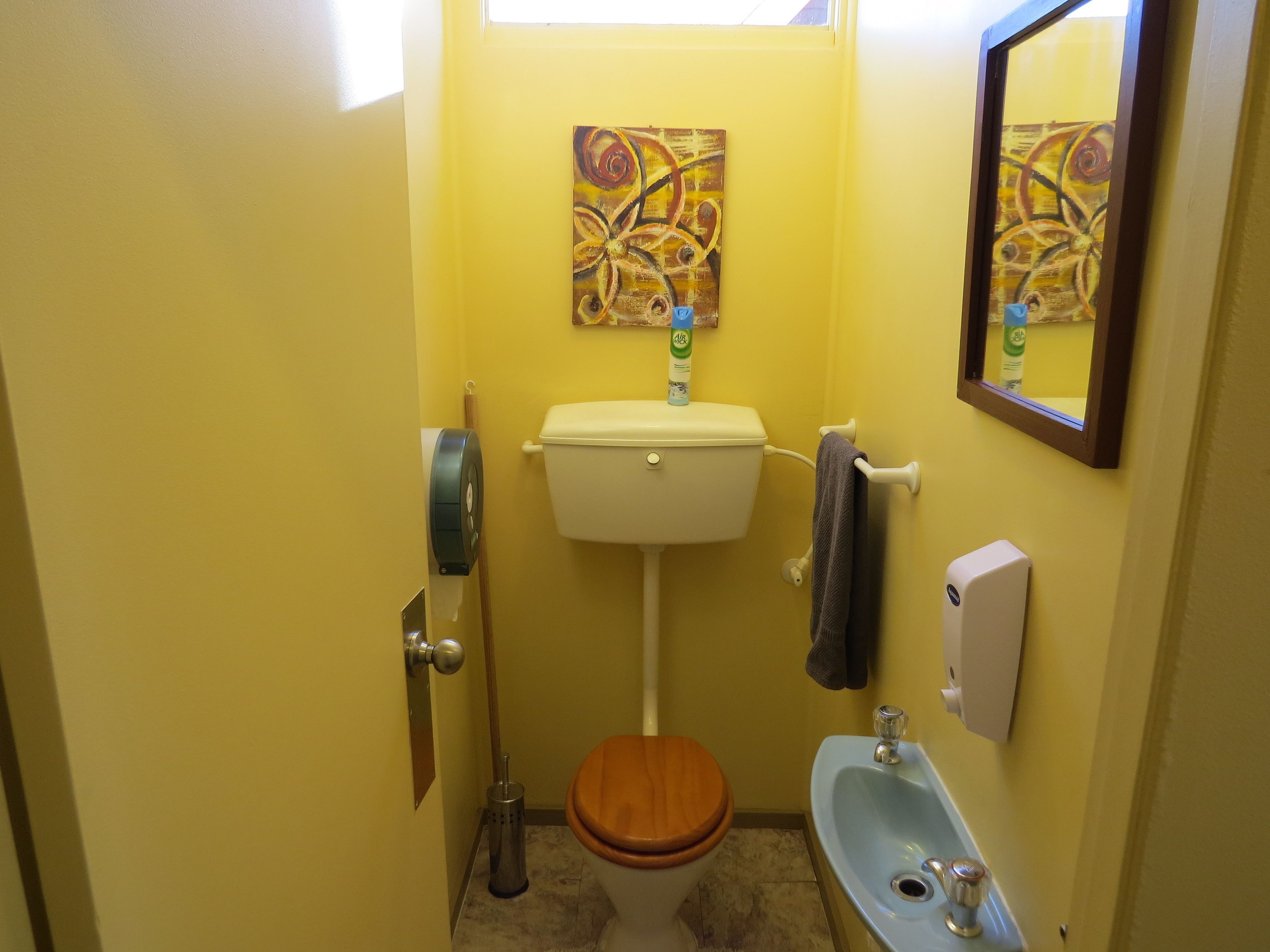 A small bathroom with a toilet, sink, and a painting on the wall.