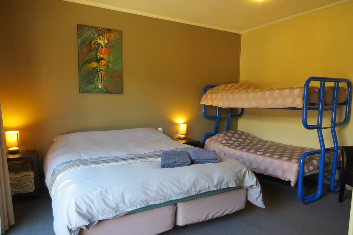 A room with a bunk bed, a single bed, and a painting on the wall.