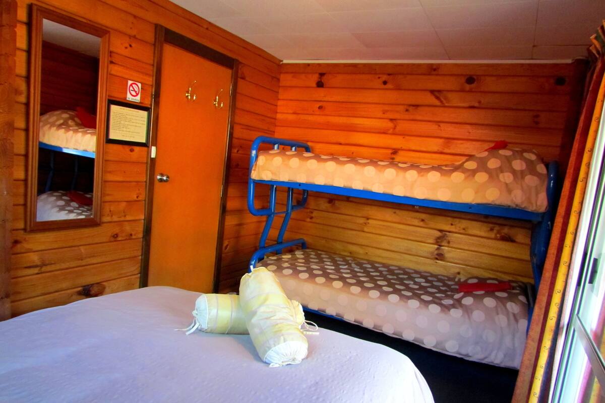 A bunk bed room with a wooden interior, a door with a 'No Smoking' sign, and a mirror on the wall.