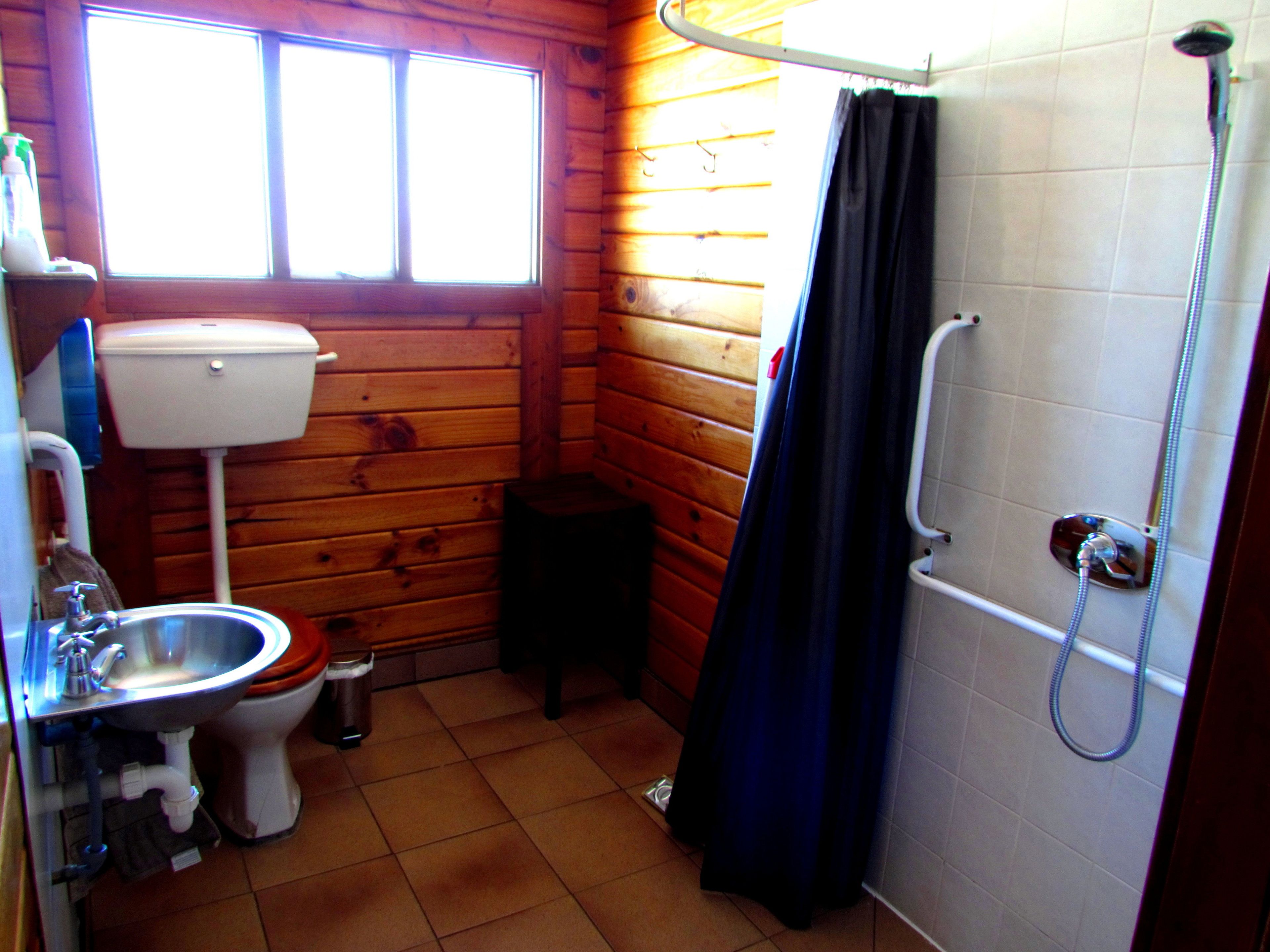 A small, wooden cabin bathroom with a toilet, sink, and shower.