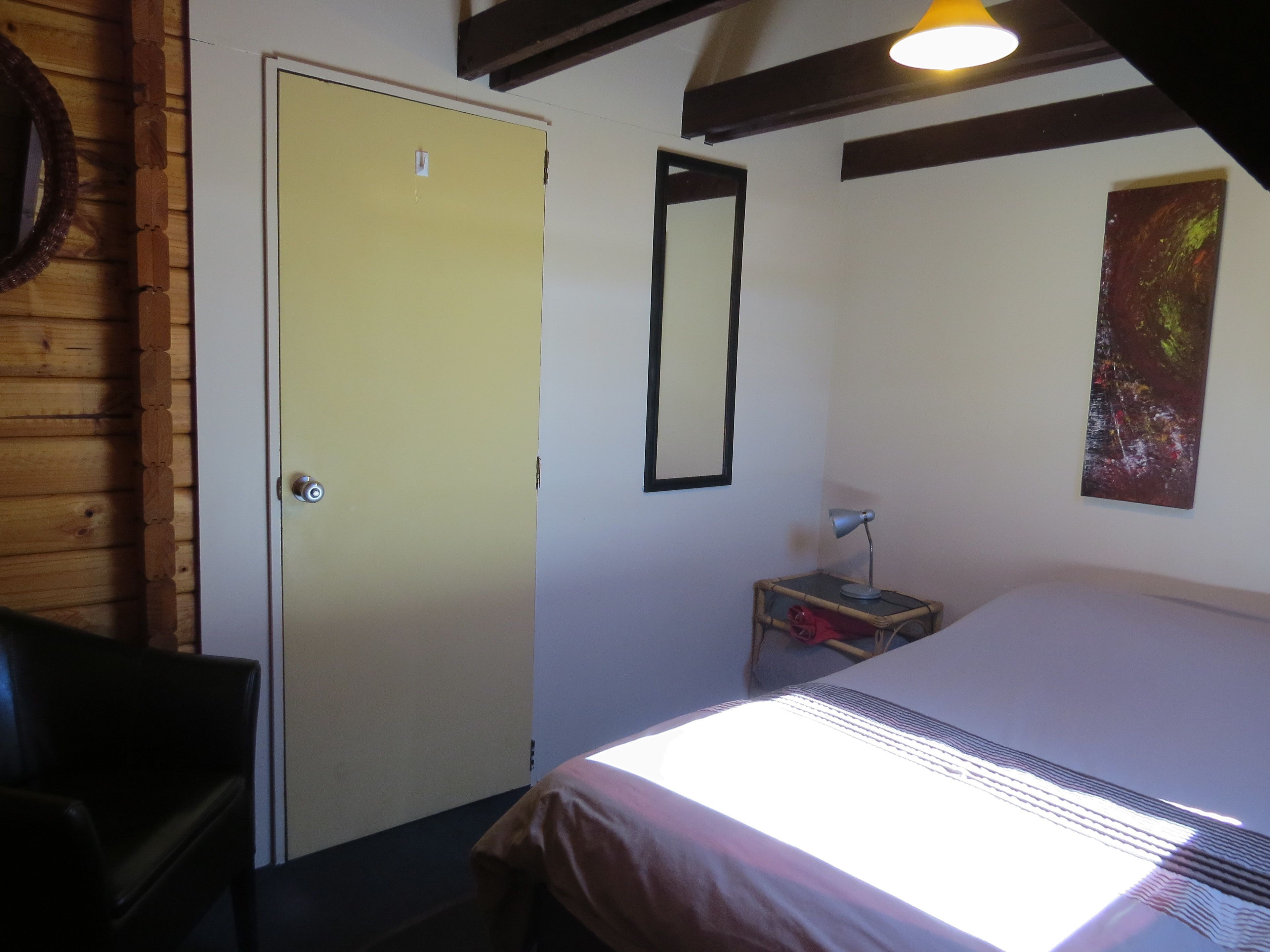 Une pièce comprenant un lit, un bureau, une chaise, une porte, un miroir, une lampe et un tableau accroché au mur.