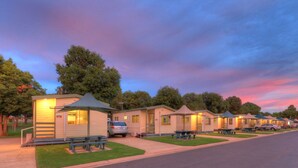 A row of mobile homes with picnic tables and a car parked in front.