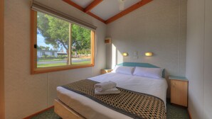 A bedroom with a large window, a bed with a checkered bedspread, a nightstand, and a wall-mounted light fixture.