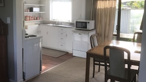 A compact kitchen with a microwave, stove, and cabinets, leading to a dining area with a table and chairs. - Whitianga Campground (Whitianga)