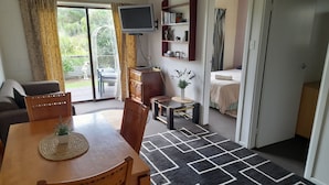 A cozy living room with a dining area, a TV mounted on the wall, and a bookshelf. - Whitianga Campground (Whitianga)