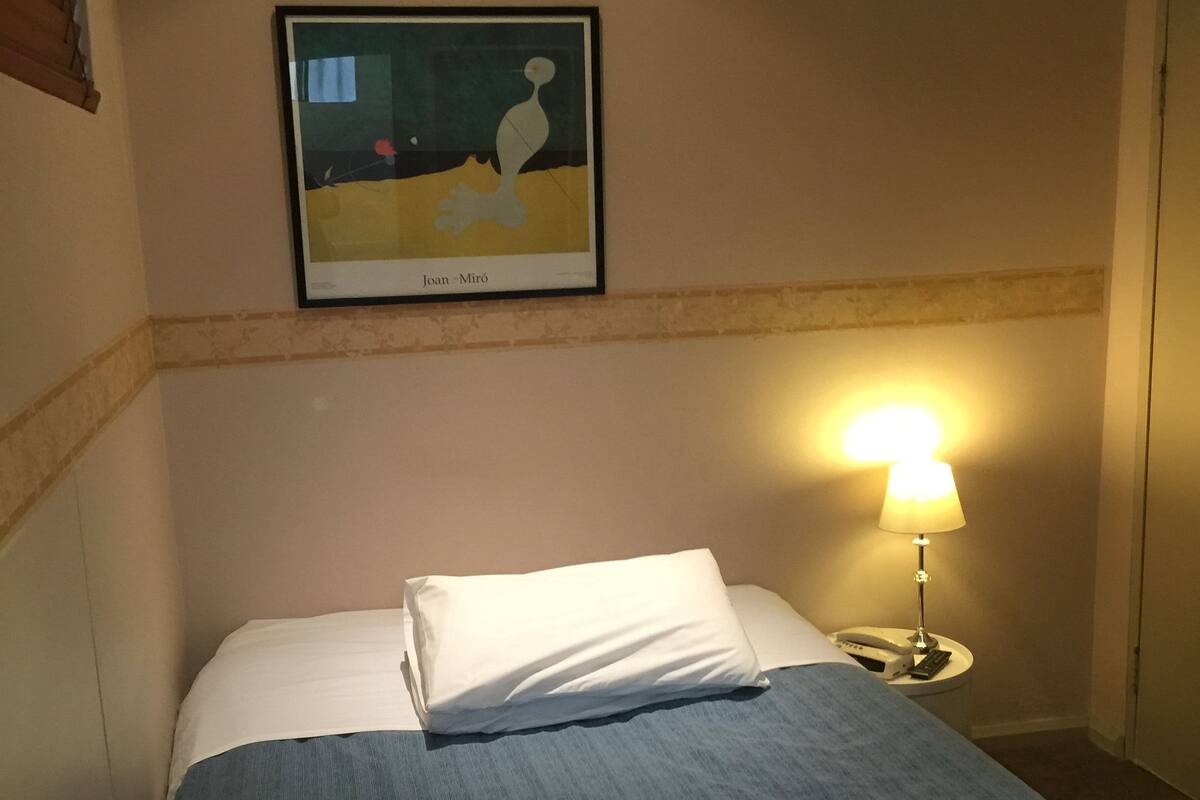 Siisti hotellihuone, jossa on huolitellusti pedattu sänky, seinällä taulu, yöpöydällä lamppu ja pienellä pöydällä puhelin.