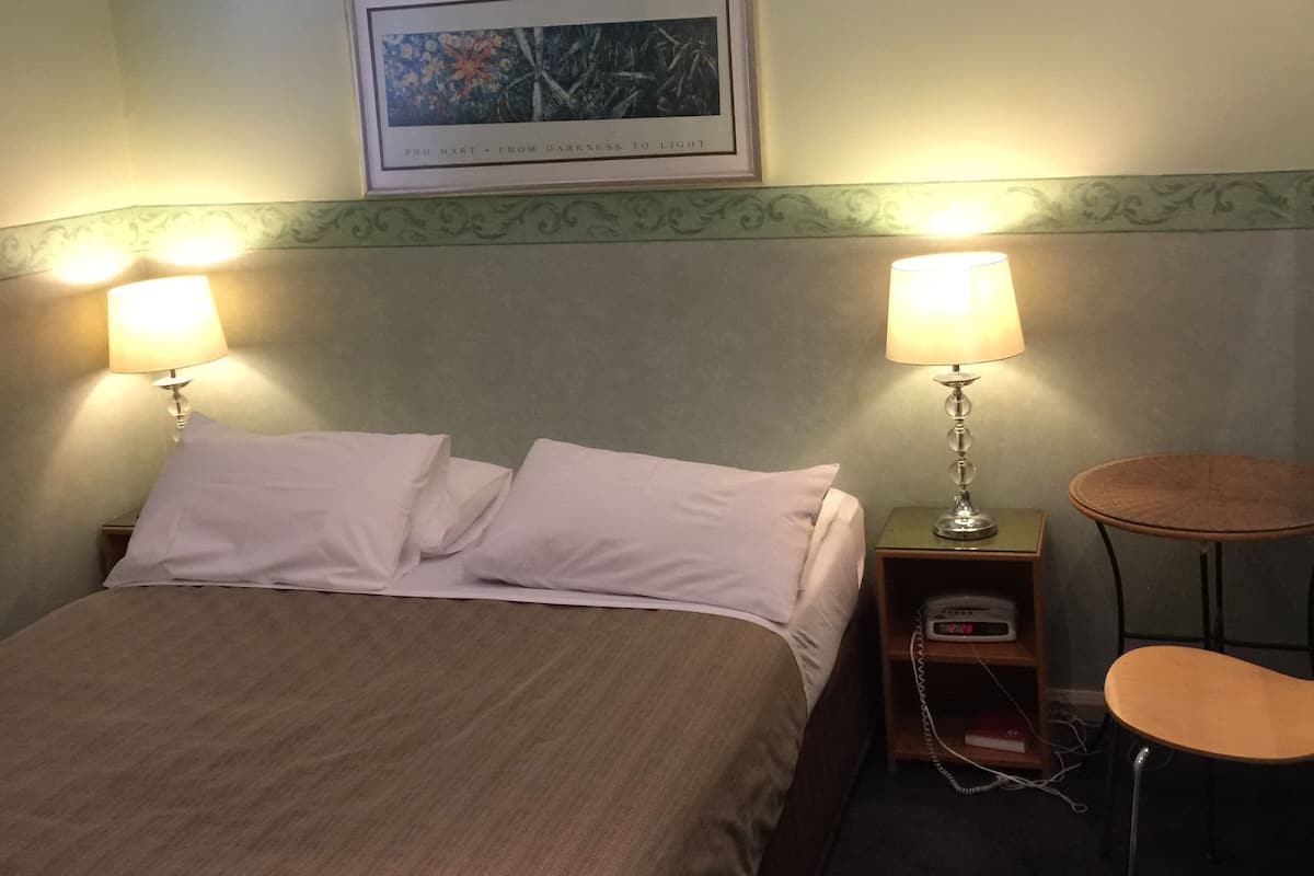 Hotellihuone, jossa on sänky, kaksi yöpöytälamppua, pieni pöytä ja kattotuuletin.