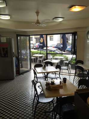 Un café avec un sol à carreaux, des tables, des chaises et un réfrigérateur orné d’une publicité pour Coca-Cola.