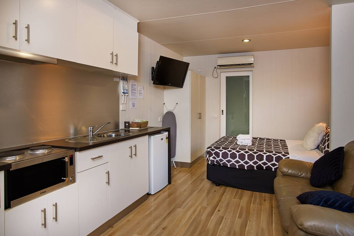 A compact kitchen with modern appliances, a small refrigerator, and a flat-screen TV mounted on the wall.
