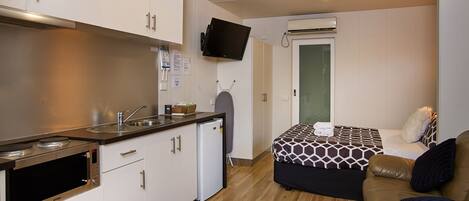 A compact kitchen with modern appliances, a small refrigerator, and a flat-screen TV mounted on the wall.