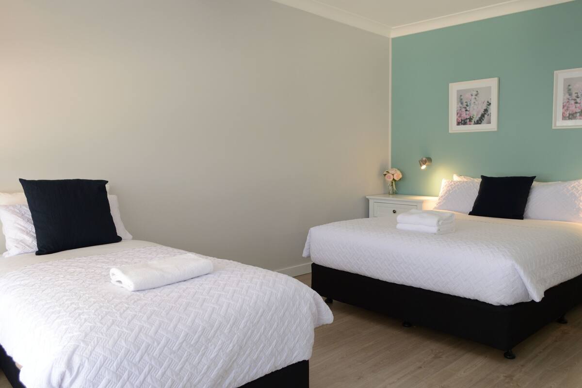 A hotel room with two beds, each with white bedding and black headboards. There are two framed floral paintings on the teal-colored wall.