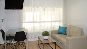 A room with a glass-top table, two black chairs, a beige sofa with a blue pillow, a white potted plant, and a flat-screen TV mounted on the wall. - Motel On Alpine (Myrtleford)