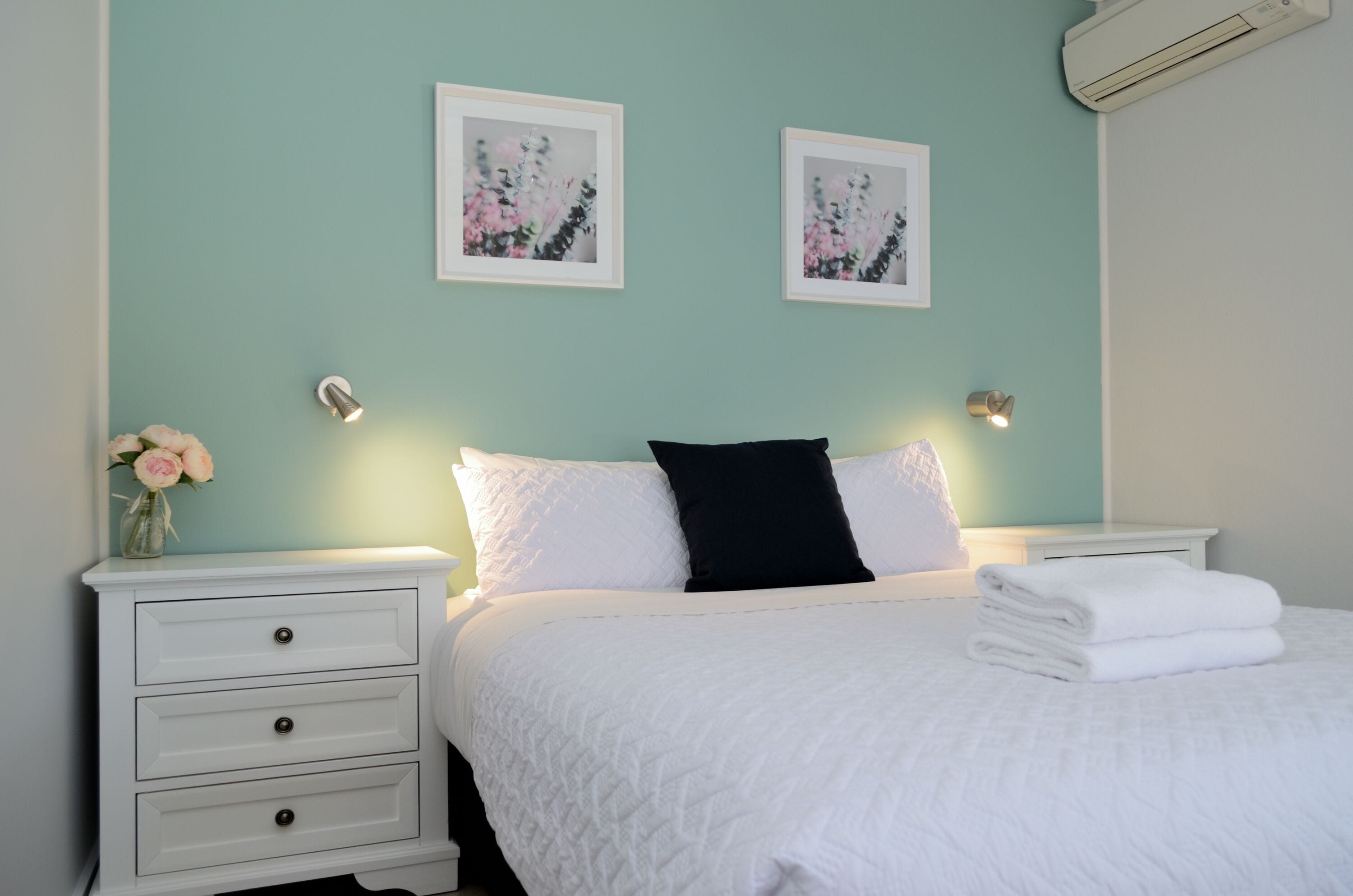 A neatly made bed with white bedding and a black pillow, flanked by two bedside tables with lamps.