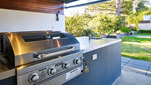A modern outdoor kitchen with a stainless steel grill, built-in sink, and wooden panel accents. - Motel On Alpine (Myrtleford)