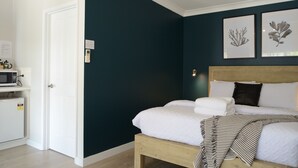 A bedroom with a bed, a wooden headboard, a white bedside table with a microwave, and two framed botanical prints on the wall. - Motel On Alpine (Myrtleford)