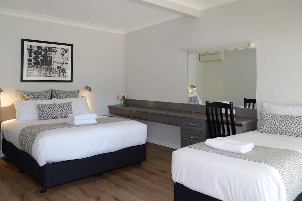 A modern hotel room with two beds, a large mirror, a desk with a chair, and a wall-mounted artwork.