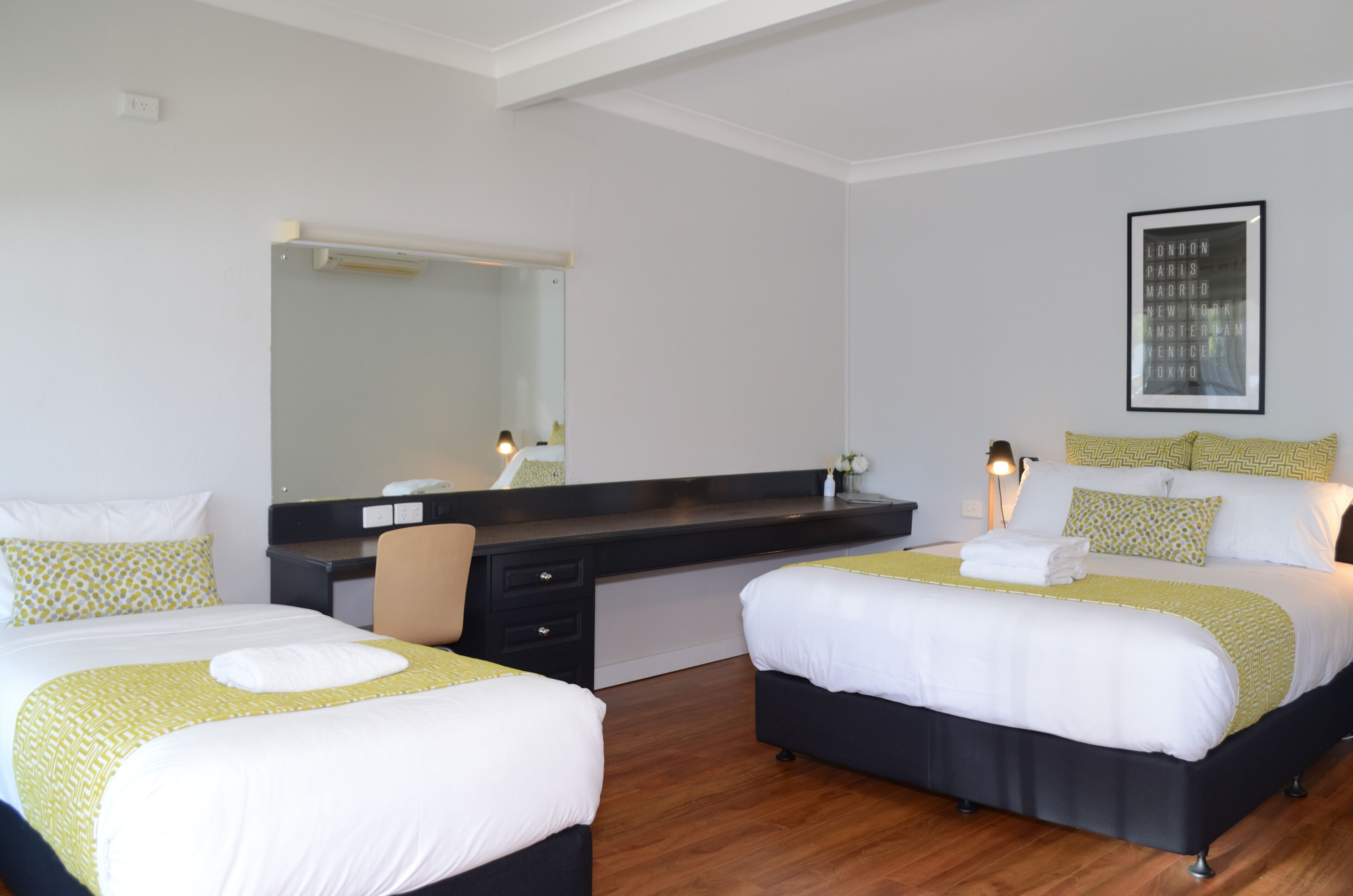 A hotel room with two beds, a desk, a chair, a mirror, and a framed picture on the wall.