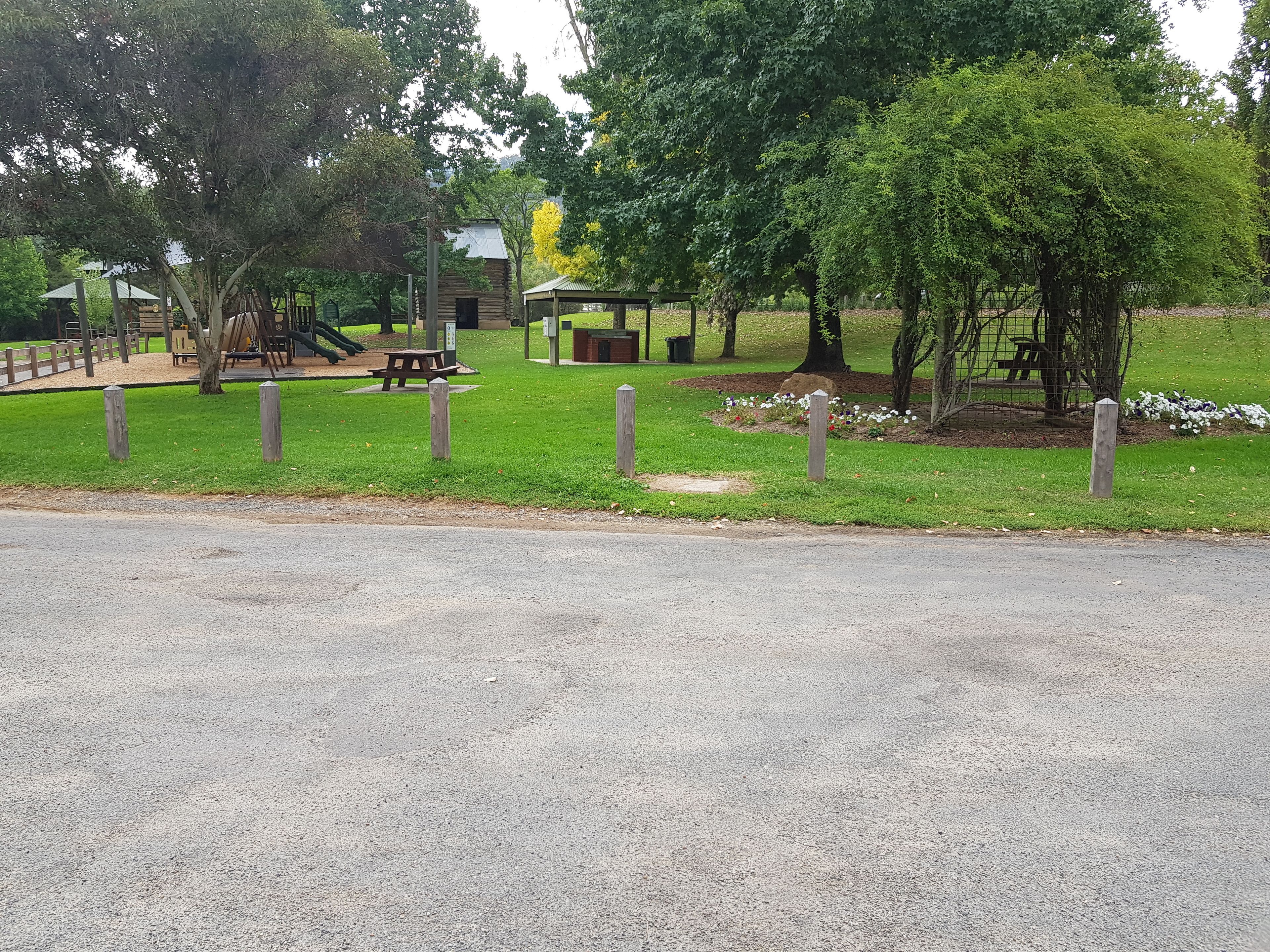 Un parque con un área de juegos, mesas de picnic y una zona vallada con flores.