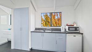 A modern kitchen with grey cabinets, a sink, a microwave, and a window with autumn leaves. - Ascot Vale Motor Lodge (Christchurch)